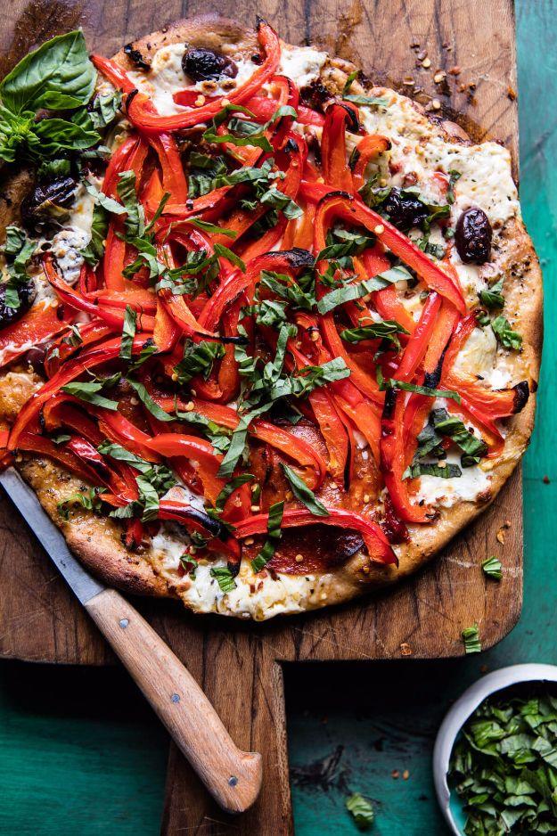 Thin crust pizza piled with thinly sliced roasted red peppers and fresh basil on a wooden board with a knife