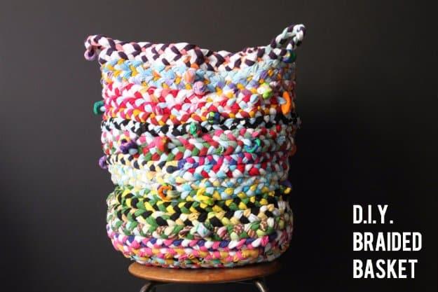 Tall coiled basket braided from multicolored t-shirt jersey strips with beads worked in, on a stool against a dark background