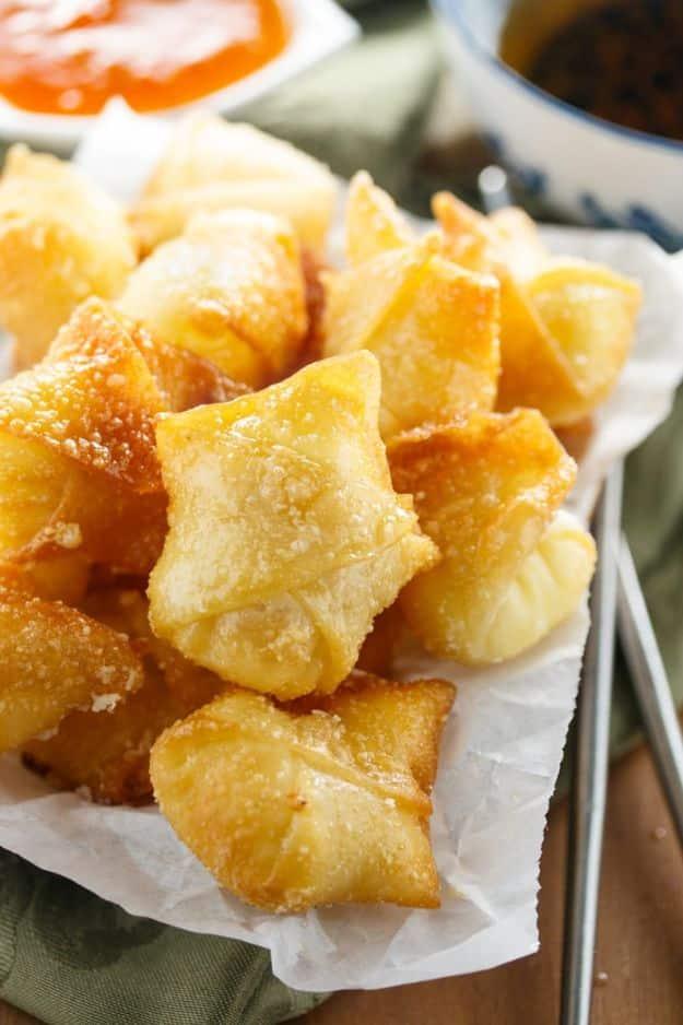 Sweet cream cheese wontons, golden fried wonton parcels on paper beside a small bowl of red dipping sauce