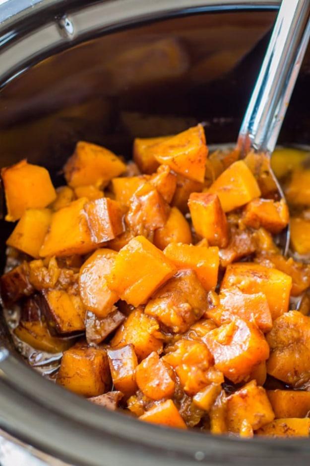 Orange butternut squash cubes in glossy cinnamon-sugar sauce with a metal spoon inside a dark slow cooker