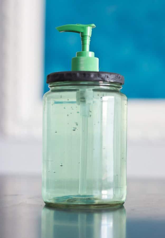 Clear pickle jar soap dispenser filled with pale gel soap and topped with a dark painted lid and a green pump