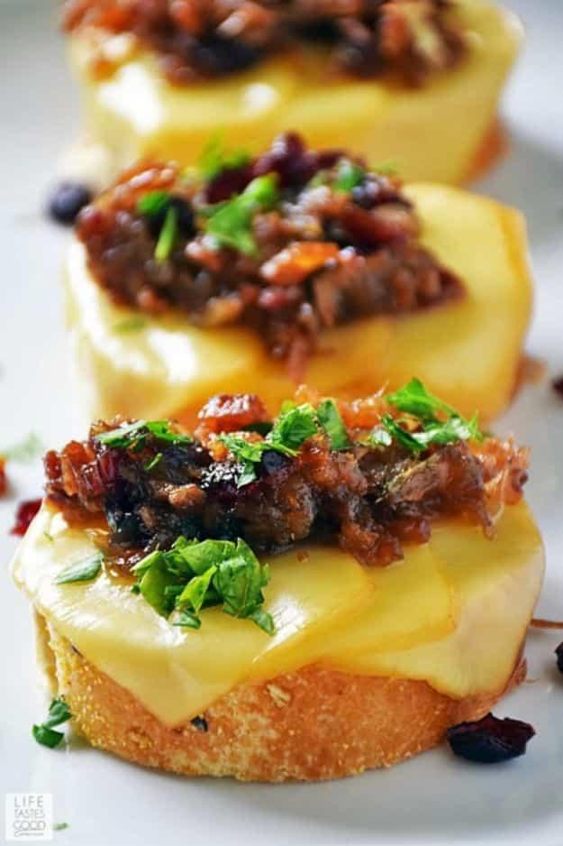 Cranberry bacon jam crostini, toasted bread topped with melted cheese and dark bacon jam with green herbs