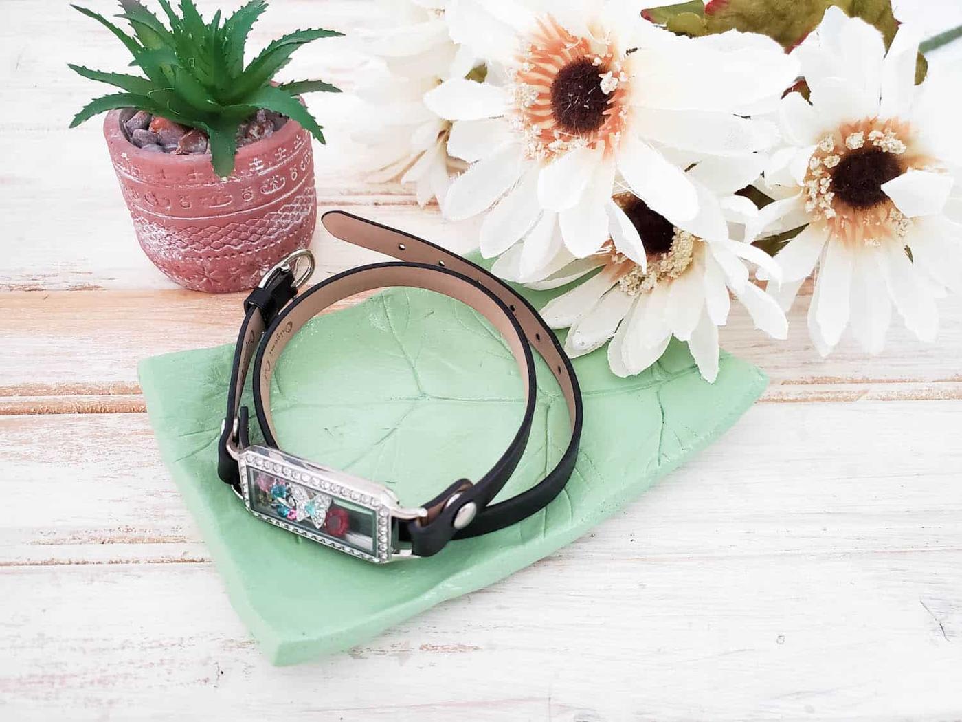 Pale green air dry clay tray imprinted with a leaf holding a watch and a bracelet, beside a small succulent and daisies