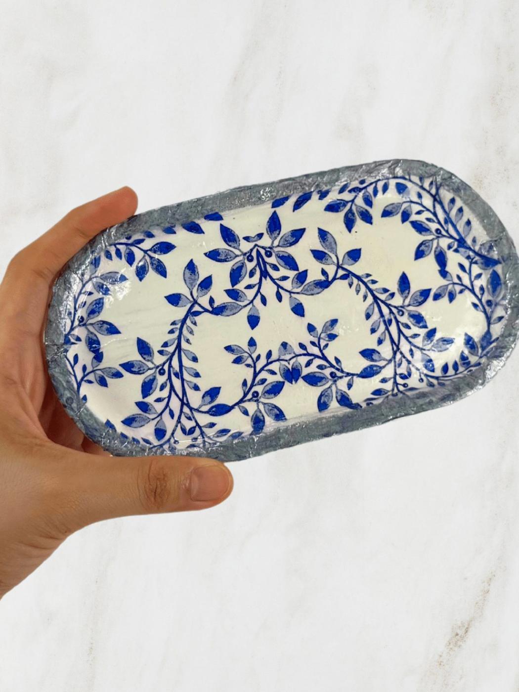 Oval blue and white patterned clay jewelry tray with a glossy finish held in one hand over a marble surface