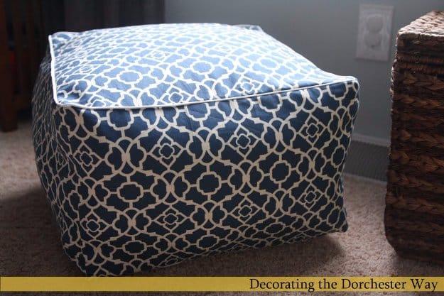 Square cube floor cushion in a navy and cream lattice print with white cording piped around the top edge on carpet