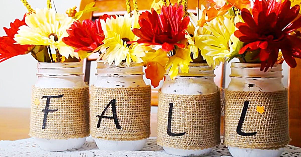 Four burlap wrapped mason jars spelling FALL in black letters, each filled with red and yellow daisies