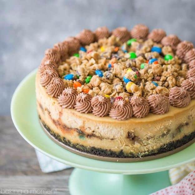 Monster cookie dough cheesecake topped with chocolate whipped cream swirls and M and Ms on a green cake stand