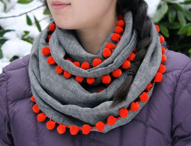 DIY clothes for winter, a grey scarf trimmed with bright red pom poms looped over a purple puffer coat in the snow