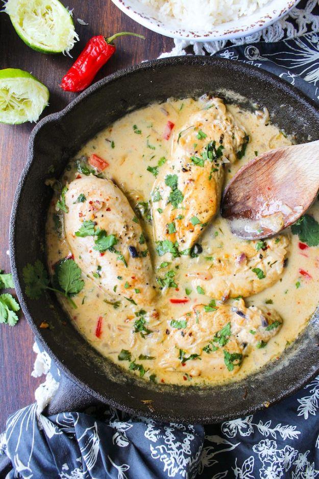 Creamy coconut lime chicken breasts in a skillet with pale sauce, cilantro, red chili and lime wedges