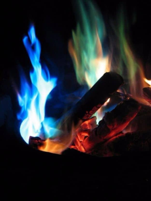 Campfire burning with bright blue and green flames over orange embers against a dark background at night