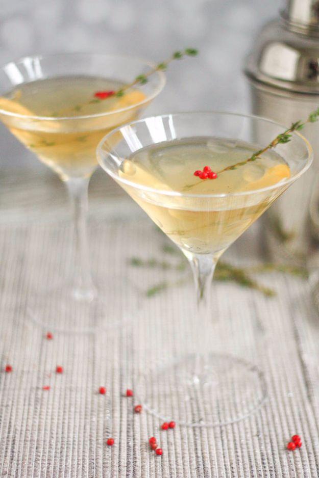 Two martini glasses of pale gold vanilla pepper and thyme martini with thyme and pink peppercorns on the cloth
