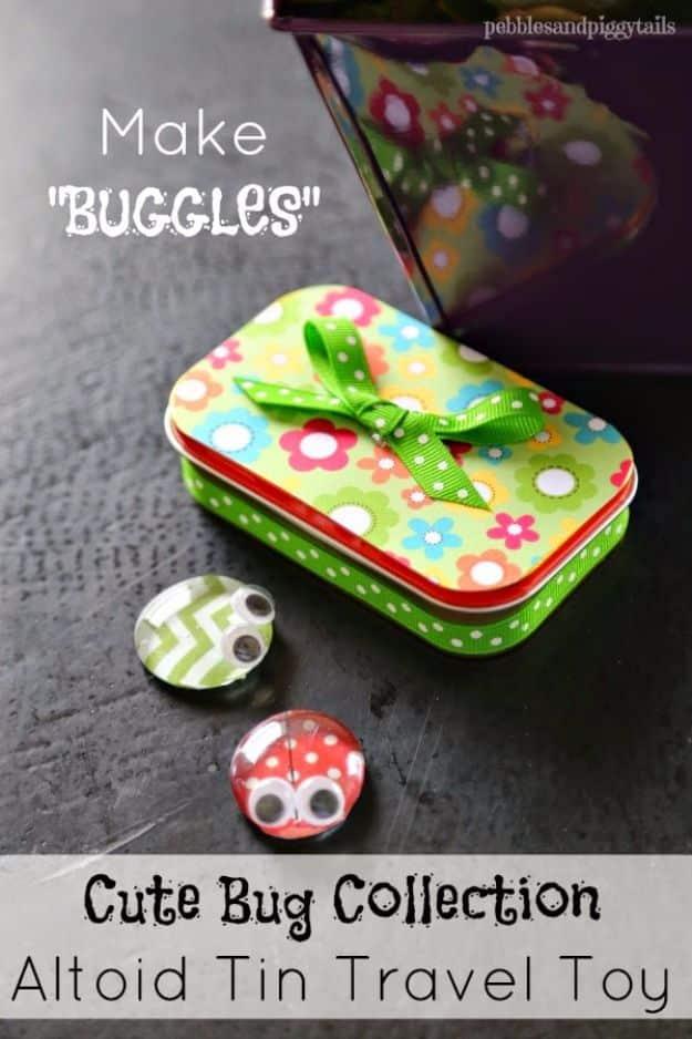 Flower patterned Altoid tin with a green ribbon bow, beside two glass gem bugs with googly eyes on a dark surface