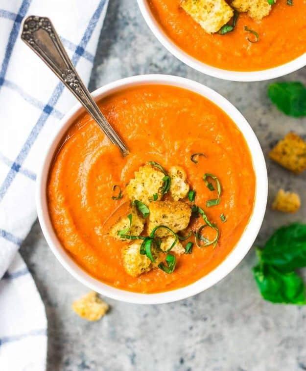 Roasted carrot soup in a white bowl, bright orange and topped with herbed croutons and shredded basil leaves