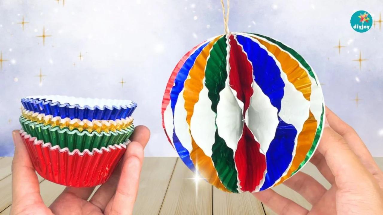 Christmas Ornaments - one hand holding a stack of metallic foil cupcake liners and the other holding the finished striped ornament ball on a jute string