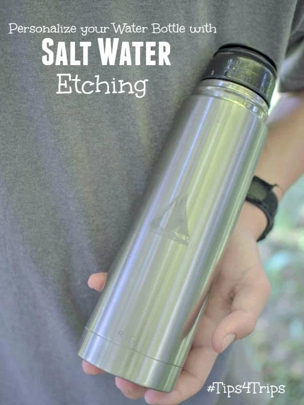 Salt water etched bottle, a brushed steel water bottle with an etched sailboat design held in front of a gray t-shirt