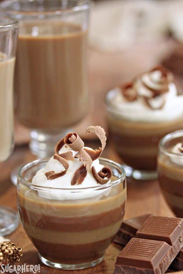 Layered coffee panna cotta in glasses showing pale and dark bands topped with whipped cream and chocolate curls