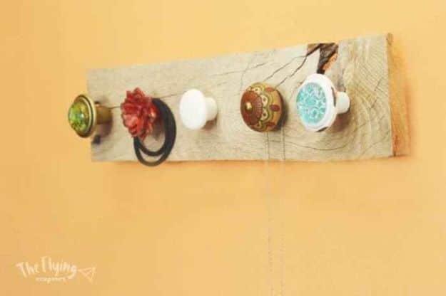 Weathered pallet board with five mismatched vintage door and cabinet knobs mounted on a mustard yellow wall
