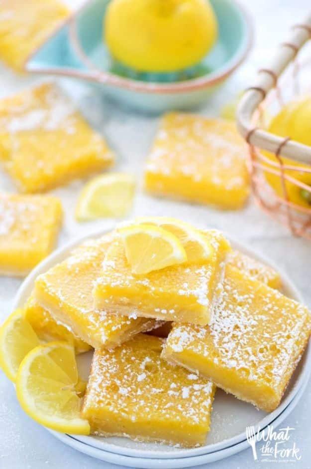 Gluten free lemon squares dusted with powdered sugar stacked on a plate with lemon slices and a juicer