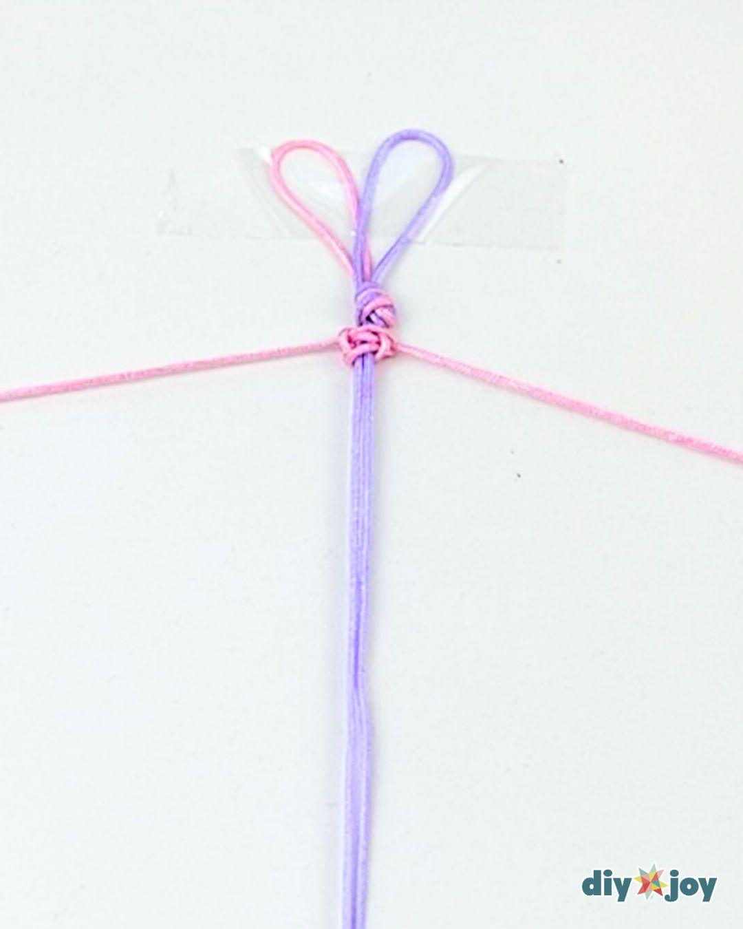 Making an easy macrame bracelet, with the pink working thread laid over the violet thread before the next knot