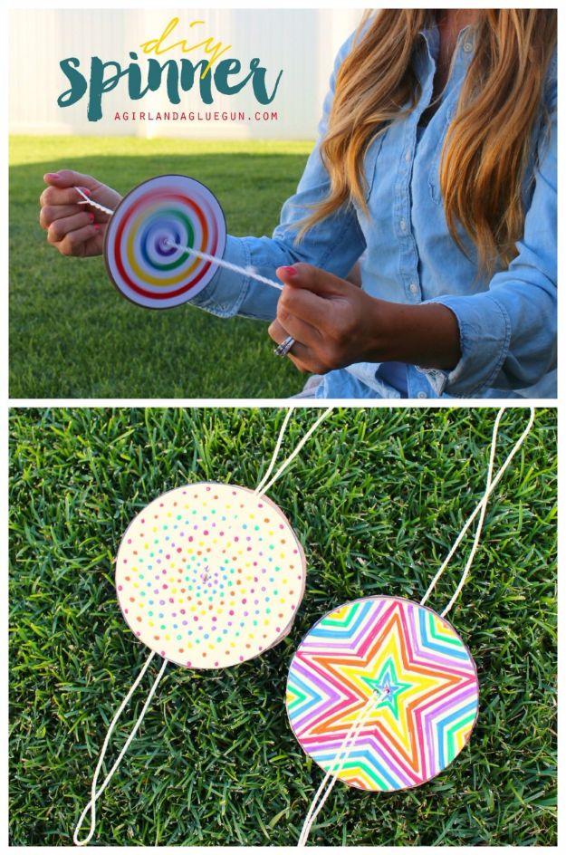 Rainbow spiral paper spinner on a white string held between two hands outdoors, with two more spinners on the grass