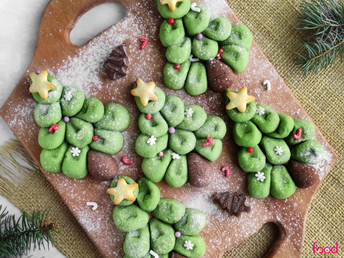 Five green pull apart Christmas tree cookies built from dough balls with brown trunks, gold stars and sprinkles on a board