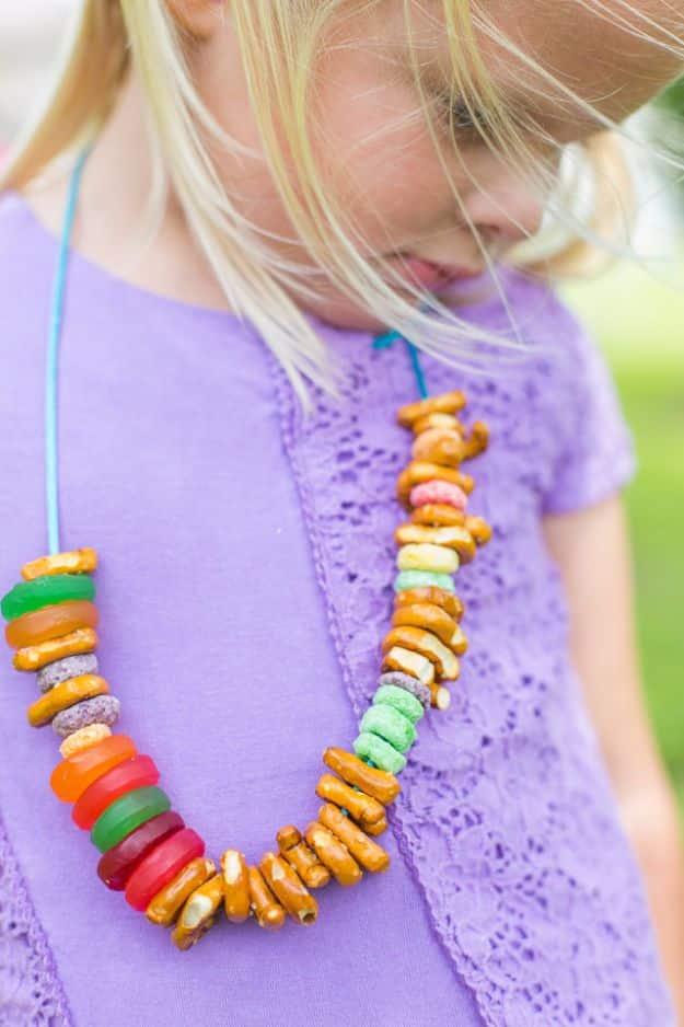 DIY picnic necklaces for kids, a child wearing a threaded necklace of cereal loops and alphabet pretzels outdoors