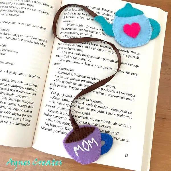 Felt teapot and teacup bookmarks joined by a long brown ribbon, lying across the printed pages of an open book