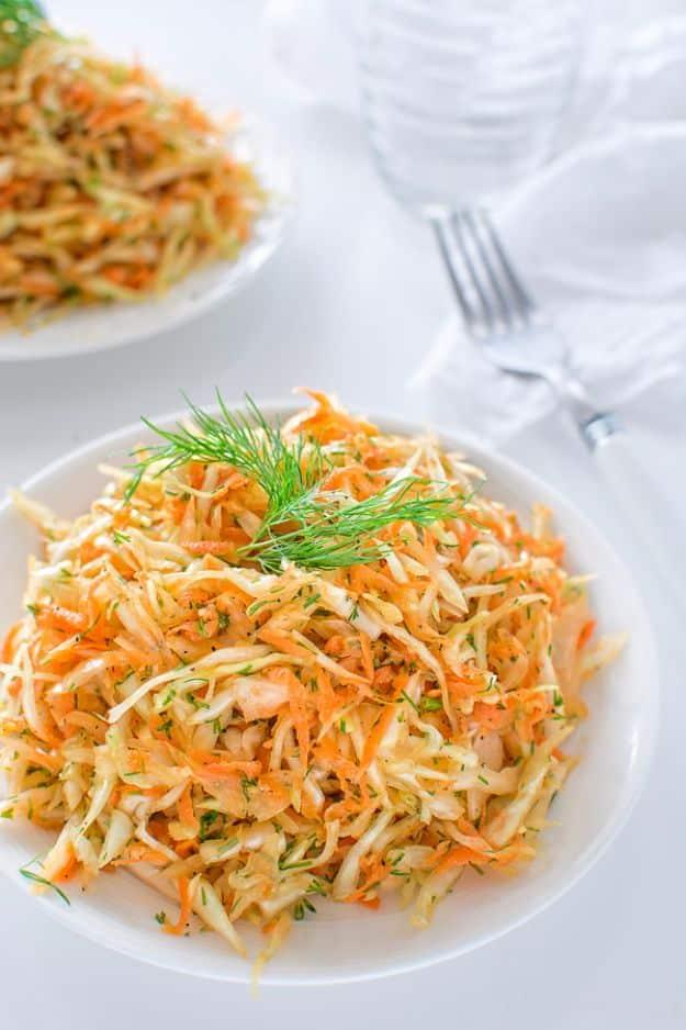 Skinny cabbage salad, finely shredded pale cabbage and orange carrot flecked with fresh dill on a white plate