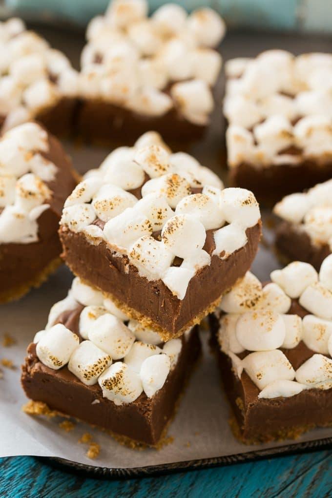 Squares of s'mores fudge with a graham cracker crust, chocolate center and toasted marshmallow top stacked on parchment