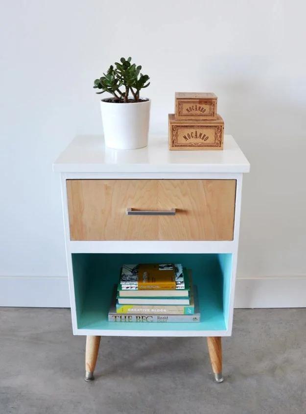White nightstand with a natural maple drawer front and bright turquoise painted cubby on splayed wooden legs, books inside
