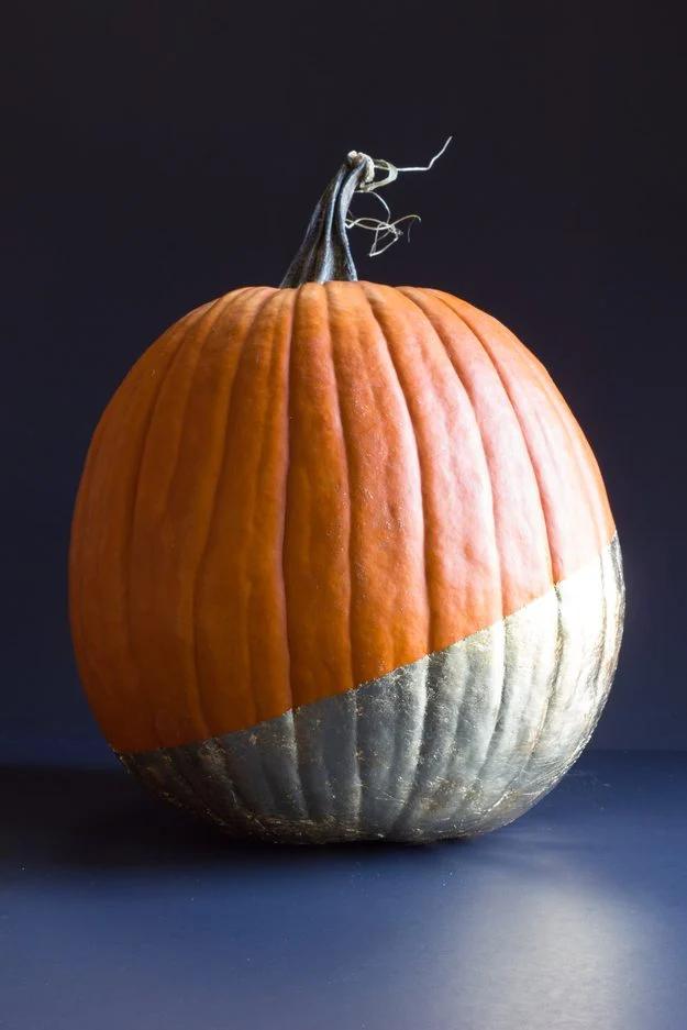 Real orange pumpkin dipped on the diagonal in gold leaf, photographed against a deep navy background