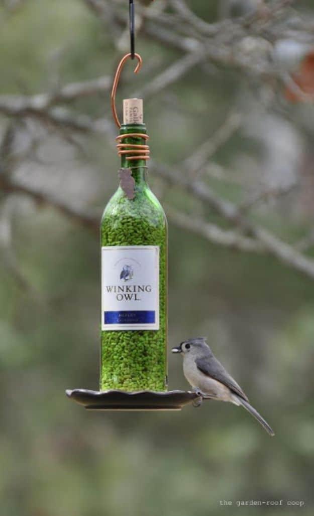 Green wine bottle bird feeder with copper wire hanger and metal saucer tray, tufted titmouse perched on the edge