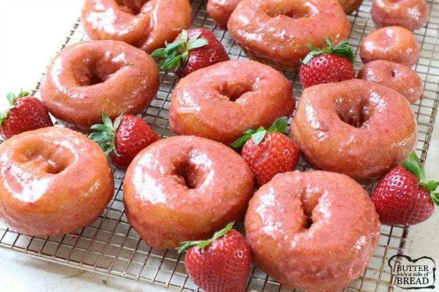 Homemade strawberry glazed donuts cooling on a wire rack with pink glaze and fresh berries scattered around