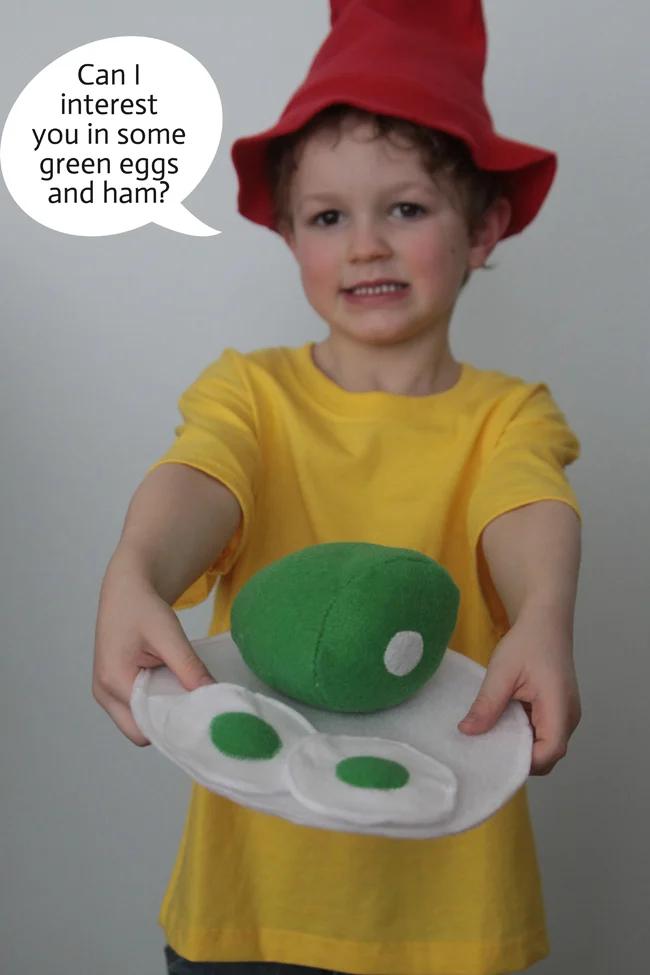 Child wearing a Green Eggs and Ham costume with a red floppy hat, yellow shirt and handmade felt plate