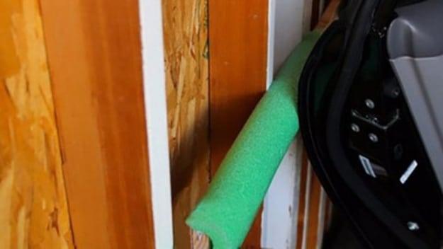 Green pool noodle screwed to a garage wall stud, cushioning an open car door in a tight parking space