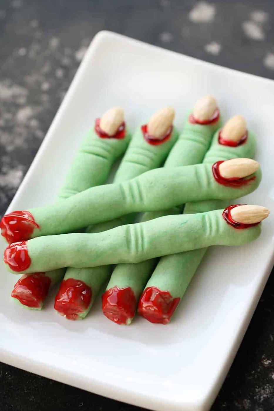 Green witch finger cookies shaped with knuckle lines and almond fingernails on a dark serving tray for Halloween