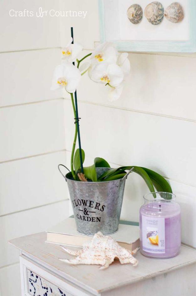 Galvanized pot with an orchid, a shell and a lavender candle styled on a white side table by shiplap