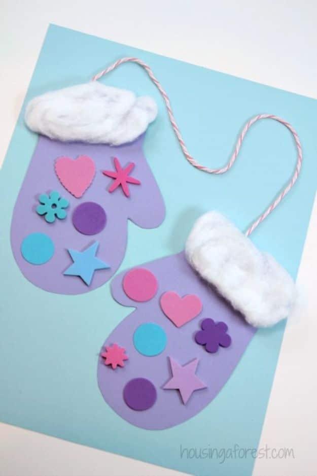 Two purple paper mittens with stretched cotton ball cuffs and foam sticker shapes, joined by white twine on blue paper