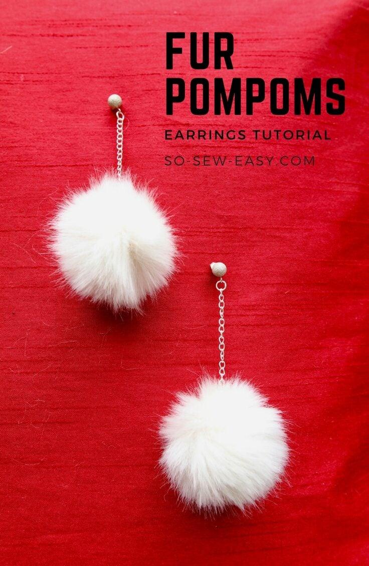 Faux fur pom pom earrings, two white fur balls on fine silver chains with small studs, on red textured fabric