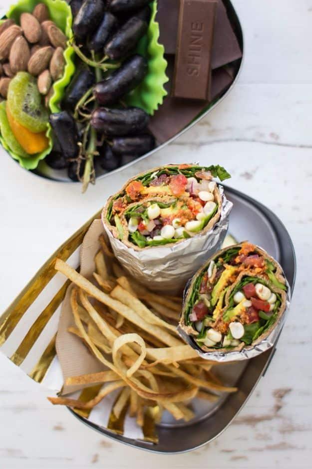 Vegan taco salad wrap cut in half and stood upright showing corn, tomato and fresh greens on a dark tray