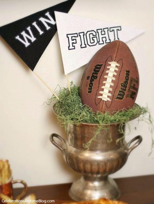 Silver trophy cup holding a football and moss, with black and white WIN and FIGHT felt pennants on sticks behind it