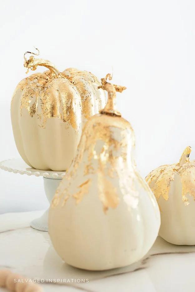 Cream chalk painted pumpkins and a gourd with gold leaf flaking down from the stems on a white cake stand