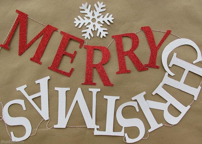 Merry Christmas banner of red and silver glitter cardstock letters on twine with a white snowflake, laid on brown paper