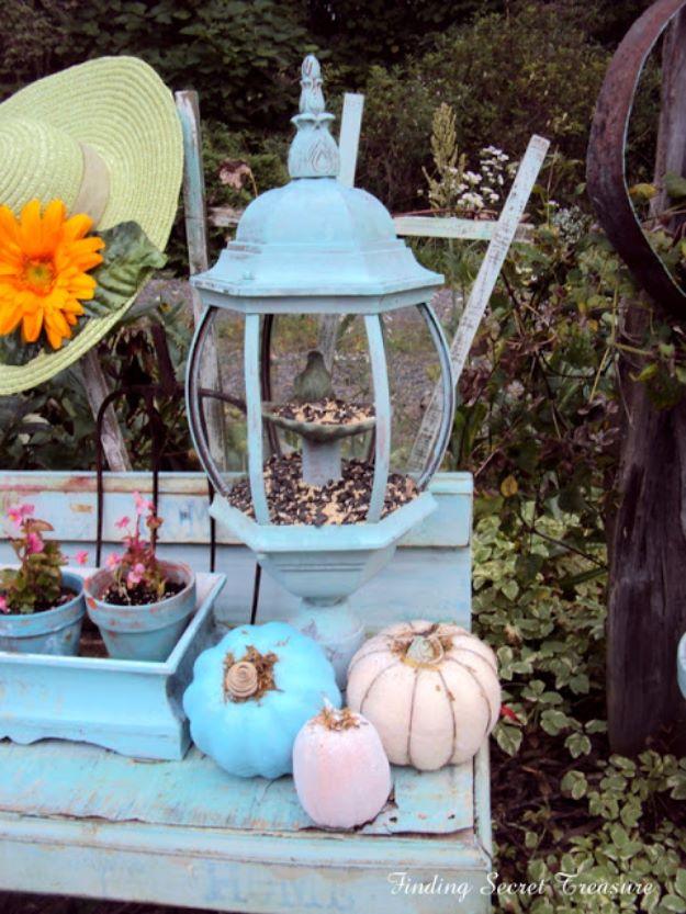 Pale aqua painted outdoor lantern fixture repurposed as a bird feeder, filled with seed, styled with pumpkins and pots