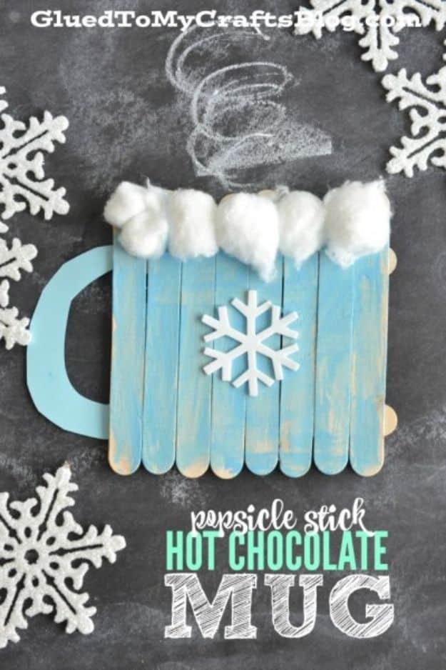 Popsicle stick hot chocolate mug craft painted pale blue with a white snowflake and cotton ball marshmallows on top