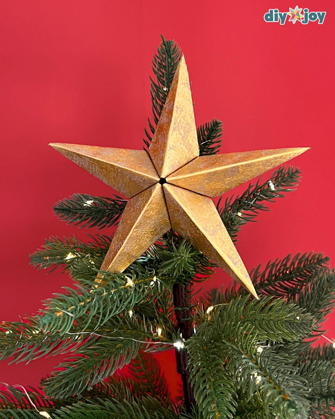 Paper bag star ornament as a tree topper, gold paper star nestled in pine with string lights at home