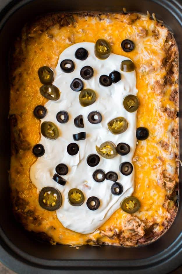 Slow cooker Texas trash beef and bean dip in a crock with melted cheese and fresh toppings over the top