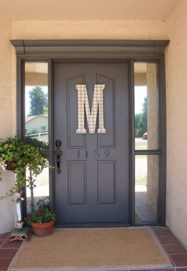 Grey painted front door with a large checked monogram letter M, house number 1159 and a potted plant