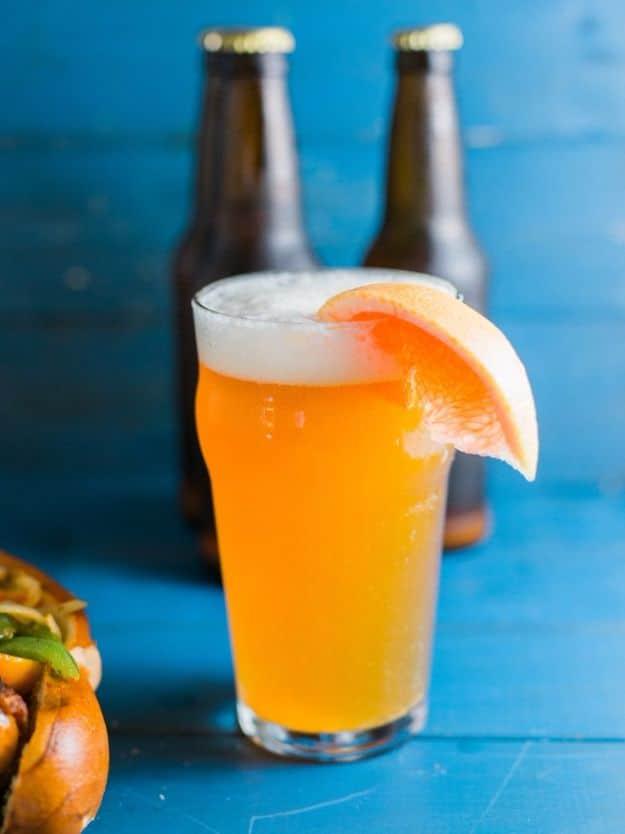 Grapefruit honey ale in a glass with a deep orange body, thick head and a wedge of fresh grapefruit brewed at home