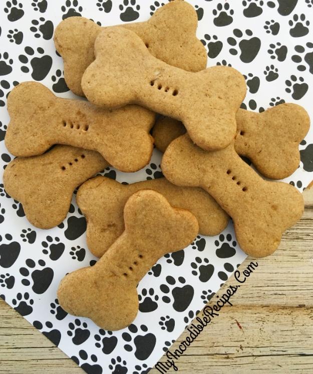 Pile of pale bone shaped dog biscuits on a black and white paw print patterned napkin on weathered white wood
